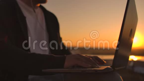 日落时分用手在笔记本电脑键盘上打字的Vault计划从高处俯瞰整个城市程序员工作视频的预览图