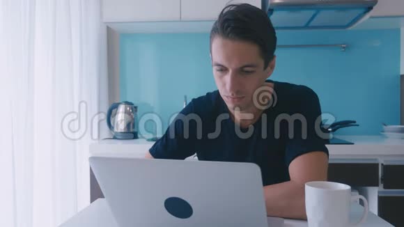 年轻的商人自由职业者在手提电脑上工作在家厨房喝咖啡视频的预览图