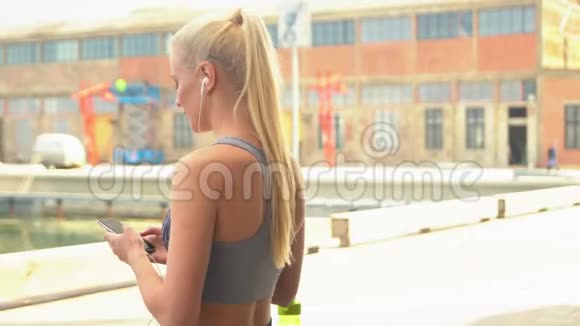 年轻迷人和运动的金发女孩穿着运动服装听音乐和放松的户外保健体育视频的预览图