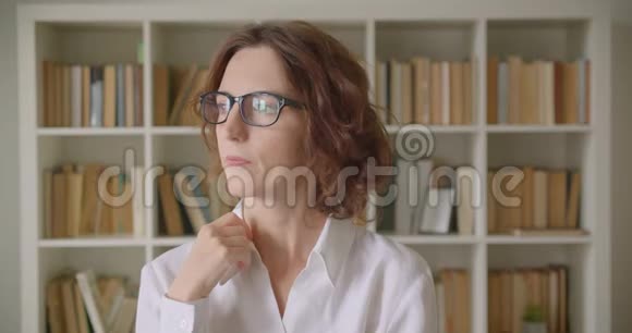 一位成年红发美女的特写肖像戴着眼镜看着室内的摄像机视频的预览图