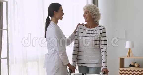 妇女照顾者帮助幸福的老残疾祖母站立步行者视频的预览图