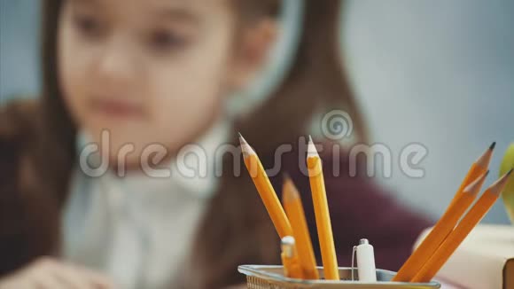 一个漂亮的女学生在灰色背景的桌子旁模糊的背景上的特写铅笔在此期间视频的预览图