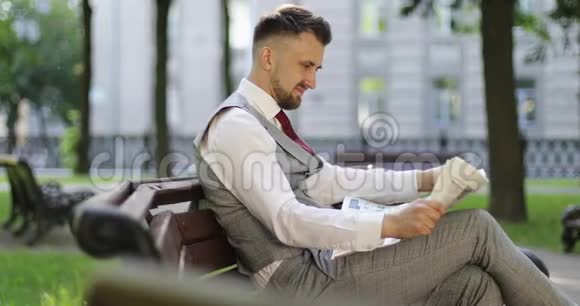 一个穿西装的富商正坐在公园里看报纸视频的预览图