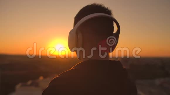 一个戴着耳机的人在日落时从摩天大楼的高度看城市一边听一边放松视频的预览图