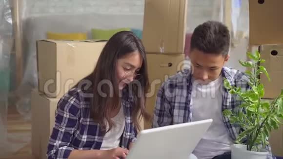 年轻的亚洲夫妇开车进了一间新公寓坐在地板上用笔记本电脑合上视频的预览图