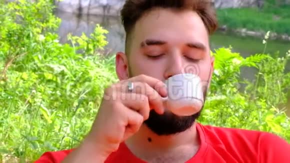 有胡子的年轻人喜欢在大自然中喝咖啡特写一个残忍的家伙手里拿着一杯白茶视频的预览图
