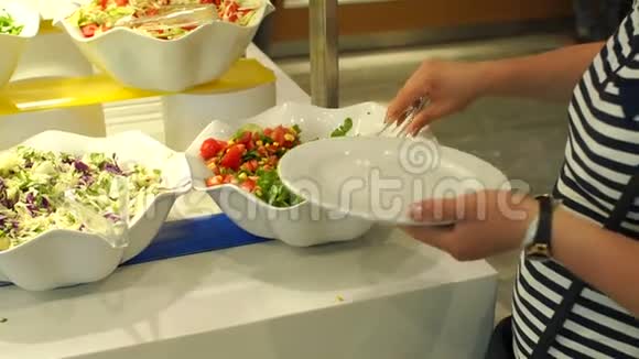 一个女人的特写把一份蔬菜沙拉放在一个带有钳子的盘子里自助服务视频的预览图
