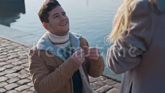 英俊的恋爱中的年轻人单膝站立拿着戒指向码头上的女朋友求婚爱家庭视频的预览图