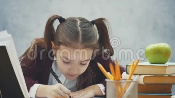 在灰色背景下关闭智能女学生在这段时间里他坐在桌子旁仔细书写视频的预览图