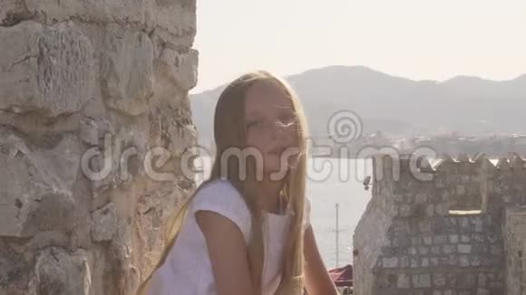 肖像美丽的女孩在石质堡垒和海洋景观上随风飘扬的头发旅游女孩正在拍摄视频的预览图