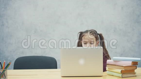 一个女学生坐在桌子旁在此期间笔记本电脑需要时间很开心在灰色背景上视频的预览图