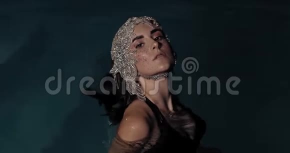 美丽的女人戴着一顶珠宝做的帽子在游泳池里摆姿势4K视频的预览图