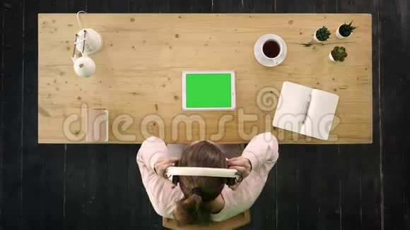 坐在办公桌前的女孩听着平板电脑里的音乐绿色屏幕模拟显示视频的预览图
