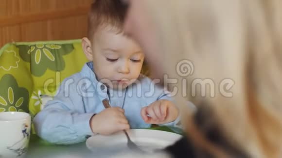 一个小男孩坐在孩子们的高椅子上桌子上放着一个带叉子的空盘子家庭视频的预览图