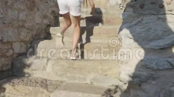 少女在石质堡垒的楼梯上行走穿着白色衣服和凉鞋在石上攀爬的旅游女孩视频的预览图