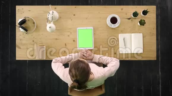 漂亮的年轻女孩坐在桌子旁的平板电脑上看视频绿色屏幕模拟显示视频的预览图