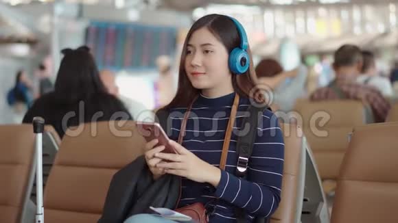 年轻的旅行者女性在机场使用智能手机和听音乐视频的预览图