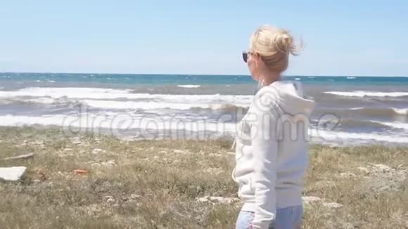 一个女孩戴着太阳镜沿着海岸线走着头发在海岸边吹着这是一个缓慢的动作稳定的画面视频的预览图