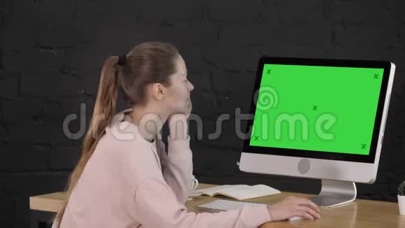 休闲迷人的年轻女人在电脑显示器前办公室的桌子上消磨时间绿色屏幕模拟视频的预览图