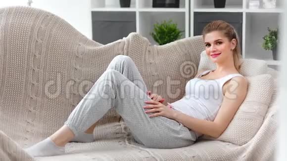 可爱的年轻女性穿着舒适的家居服在家放松躺在沙发上全镜头视频的预览图