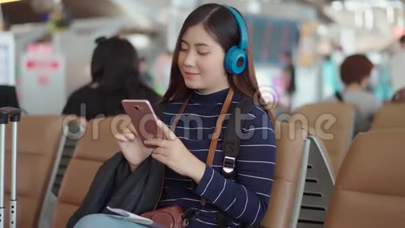 年轻的旅行者女性在机场使用智能手机和听音乐视频的预览图
