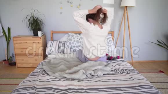 一个躺在床上的年轻女孩一大早就在舒适而简单的斯堪的纳维亚内部扎头发视频的预览图