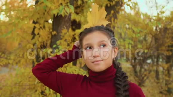 在秋天公园里戴着辫子的布鲁内特女孩像女王一样把枫叶抱在头后有黄色肖像的少女视频的预览图