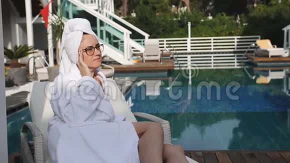 戴眼镜的女人和一件白色外套坐在游泳池旁欣赏日落视频的预览图