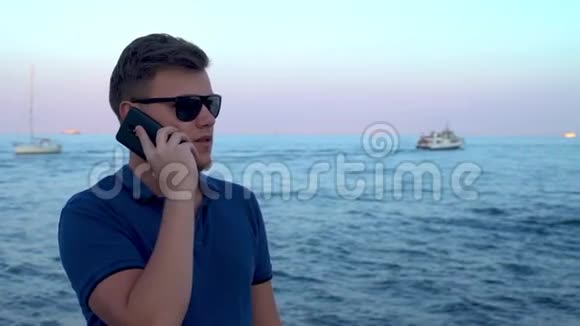 年轻有魅力的男子通过手机在Seafront通过智能手机聊天平静的蓝色黑海海滩船只驳船马达视频的预览图