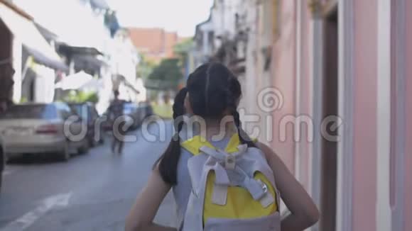 亚洲小女孩背着背包悠闲地走在普吉岛殖民地风格建筑的小径上视频的预览图