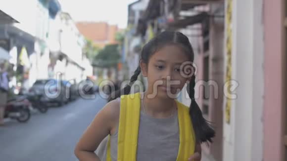 亚洲小女孩带着背包悠闲地走在普吉岛殖民地风格建筑之间的小径上夏天视频的预览图