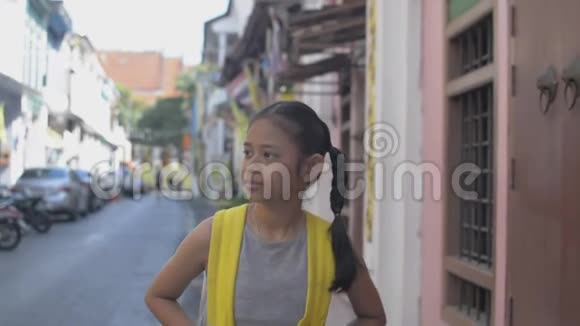 亚洲小女孩带着背包悠闲地走在普吉岛殖民地风格建筑之间的小径上夏天视频的预览图