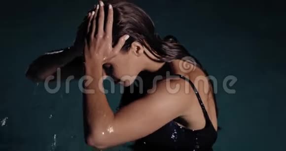 身穿黑衣的女人站在泳池里摆着姿势傍晚时分她的身上有灯光视频的预览图