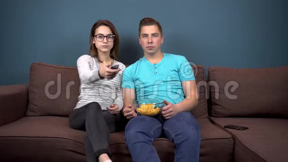 一男一女正在看电视一对年轻夫妇坐在沙发上吃薯片带有芯片的玻璃板视频的预览图