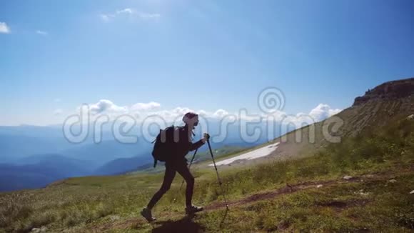 带着背包和徒步旅行杆的年轻女子走上山顶迎着蓝天慢动作夫人视频的预览图