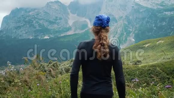 山上的长发男子徒步旅行者举起双手欣赏美丽的风景和周围的高山草地对抗岩石视频的预览图