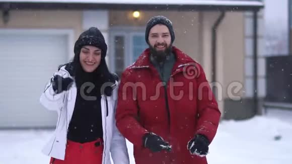 年轻的积极夫妇站在后院的大房子前面下着大雪有胡子的人视频的预览图