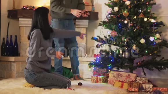 男人和女人在现代房间里装饰圣诞树女孩给玩具男人把它们挂在树枝上快乐夫妻视频的预览图