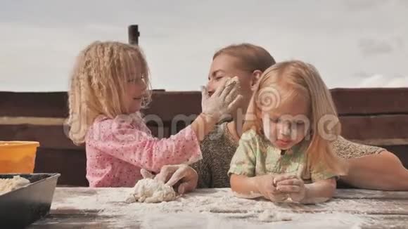 两个女儿在妈妈旁边用手揉面团用面粉把她弄脏和妈妈一起玩视频的预览图
