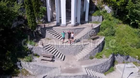 三位快乐的游客挥舞着双手在岩石中神奇洞穴的楼梯上跳跃鸟瞰视频的预览图