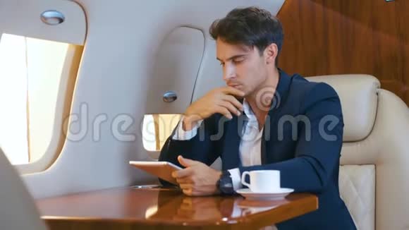 年轻的商人在笔记本电脑上工作在私人飞机上喝咖啡成功的生意视频的预览图