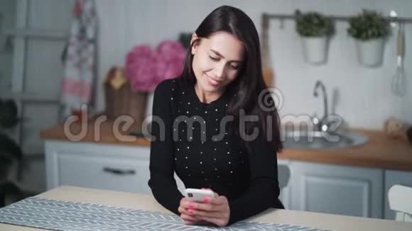 坐在厨房里用电话上网聊天或远程工作的年轻女子视频的预览图