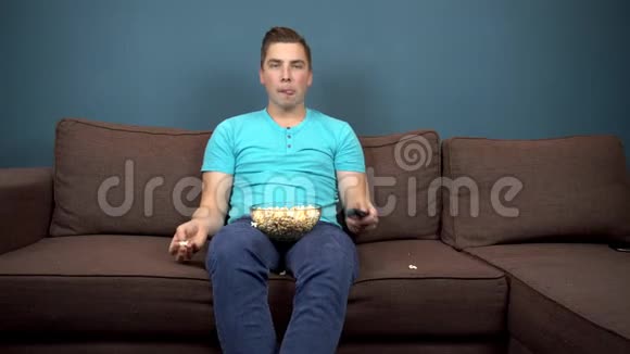 一个年轻人正在看电视和吃爆米花那家伙用嘴抓爆米花坐在沙发上观点视频的预览图