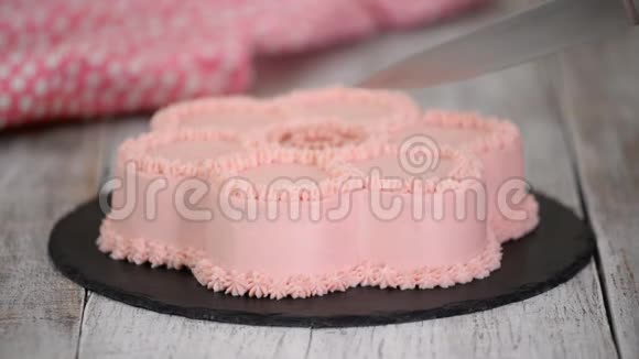 女人她的手用粉红色奶油把蛋糕切成一朵花的形状视频的预览图