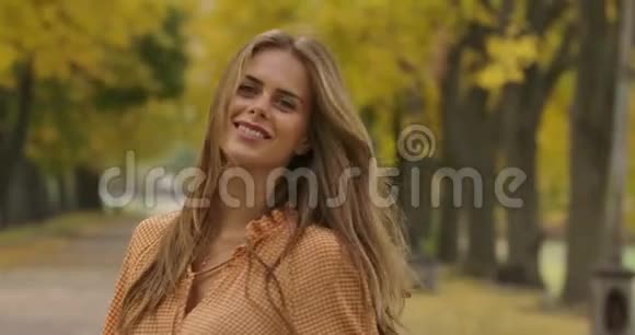 微笑的白人妇女棕色长发和绿色的眼睛在秋天的公园旋转穿着芥末衣服的优雅女孩视频的预览图