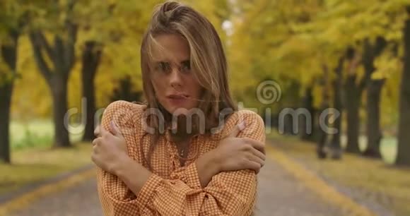 寒冷的白人女孩棕色的头发和愉快的微笑站在道路上的秋天公园是个漂亮女人视频的预览图
