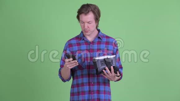 快乐的年轻潮男拿着虚拟现实耳机一边用手机视频的预览图