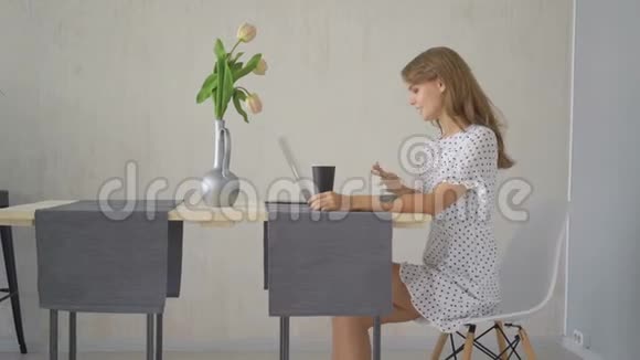 年轻女孩在家里的客厅里的一张桌子上在线上输入笔记本电脑视频的预览图