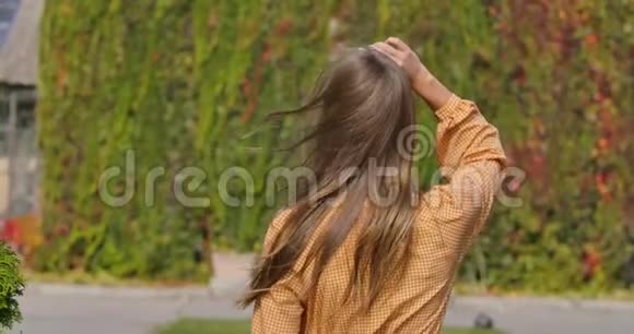 一个年轻的白种人女人穿着带有鹅脚印的芥末衣服风吹起飘逸的棕色长发视频的预览图