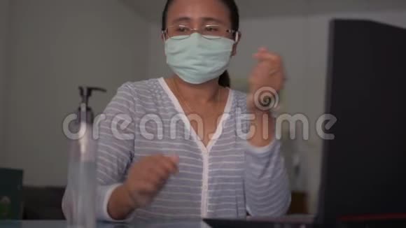 亚洲妇女戴着防护面罩将洗手液分发到手中然后用笔记本电脑在桌子上工作视频的预览图